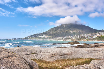 Buy stock photo Beautiful landscape of a beach near a mountain in a coastal city with a cloudy blue sky in summer. Big rocks in the sea surrounded by nature in an urban town. The coastline of the Atlantic ocean