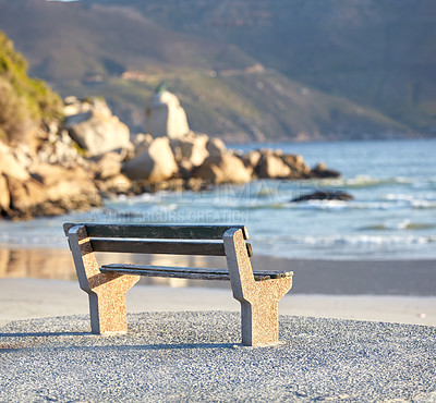 Buy stock photo Beautiful relaxing view of the ocean with a bench at the beach on a summer day. The landscape of the sea shore with big rocks and calm waves on a peaceful spring afternoon on the coastline