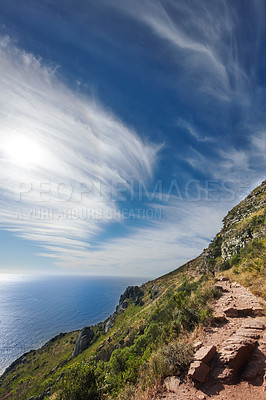 Buy stock photo Copy space with scenic coast and rocky mountain slope with cloudy blue sky background. Rugged landscape of plants growing on a cliff by the sea with hiking trails to explore in Cape Town South Africa