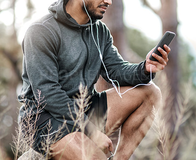 Buy stock photo Shot of a sporty young man wearing earphones while using a cellphone outdoors