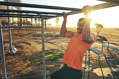 Buy stock photo Shot of a young man working out at the outdoor gym at the park