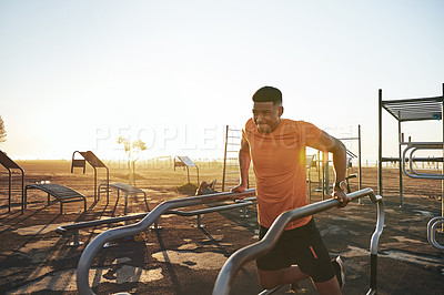Buy stock photo Shot of a young man working out at the outdoor gym at the park