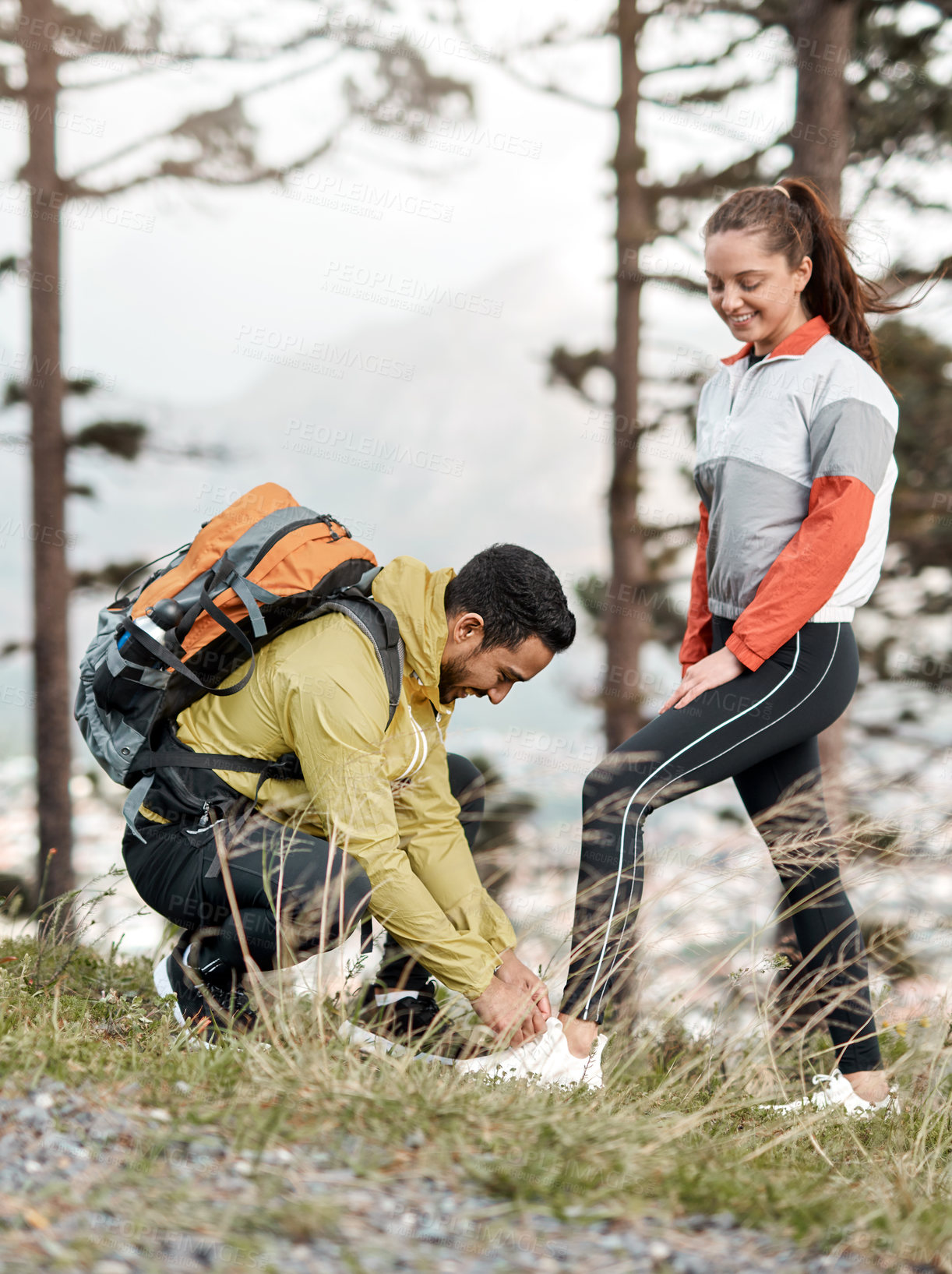 Buy stock photo Full length shot of a handsome young man tying his friend's shoelaces while on a hike in the woods