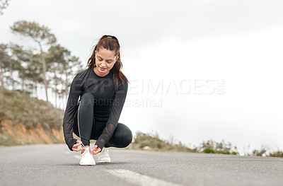 Buy stock photo Full length shot of an attractive young woman tying her shoelaces before exercising outdoors alone