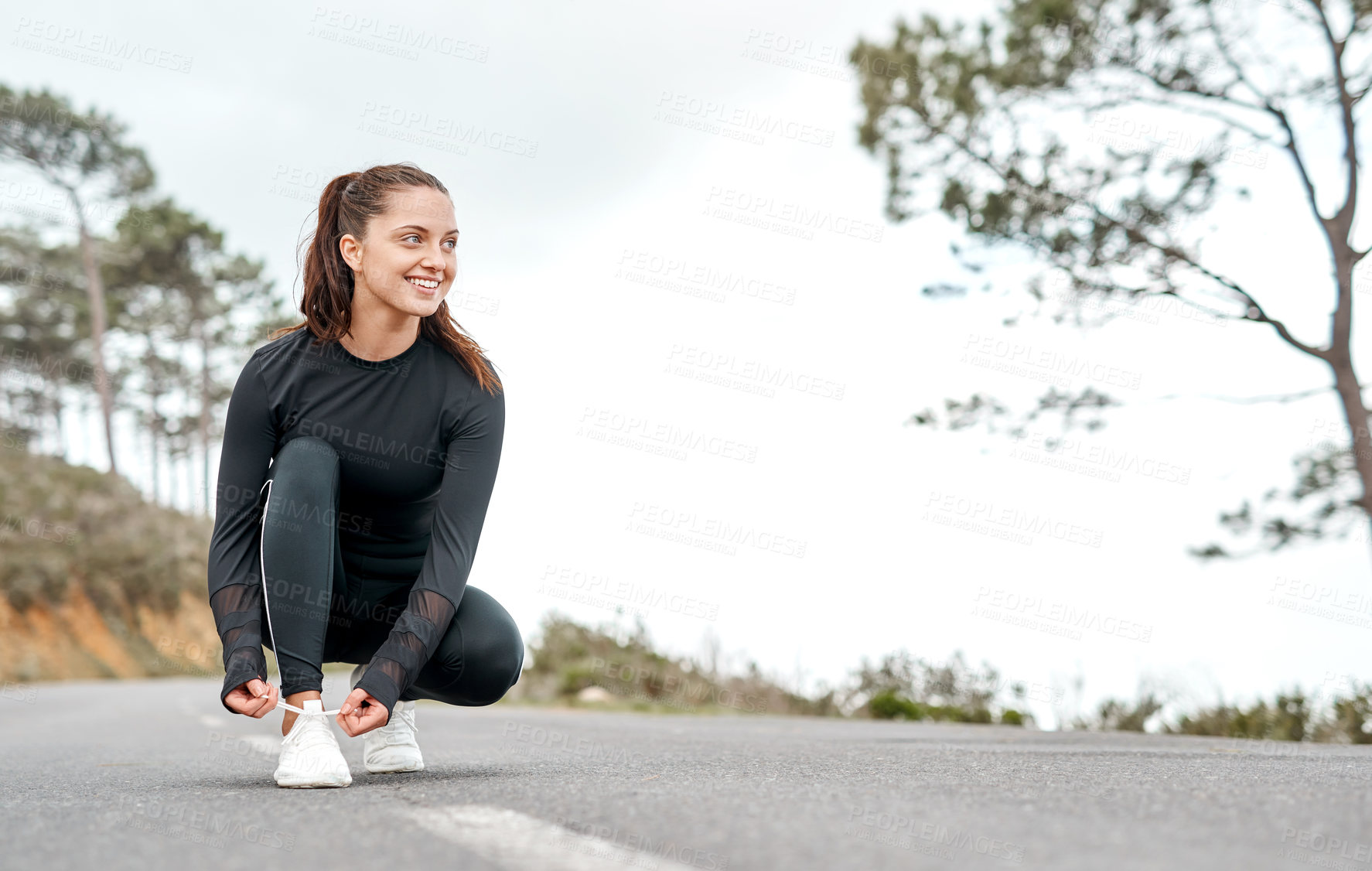 Buy stock photo Full length shot of an attractive young woman tying her shoelaces before exercising outdoors alone