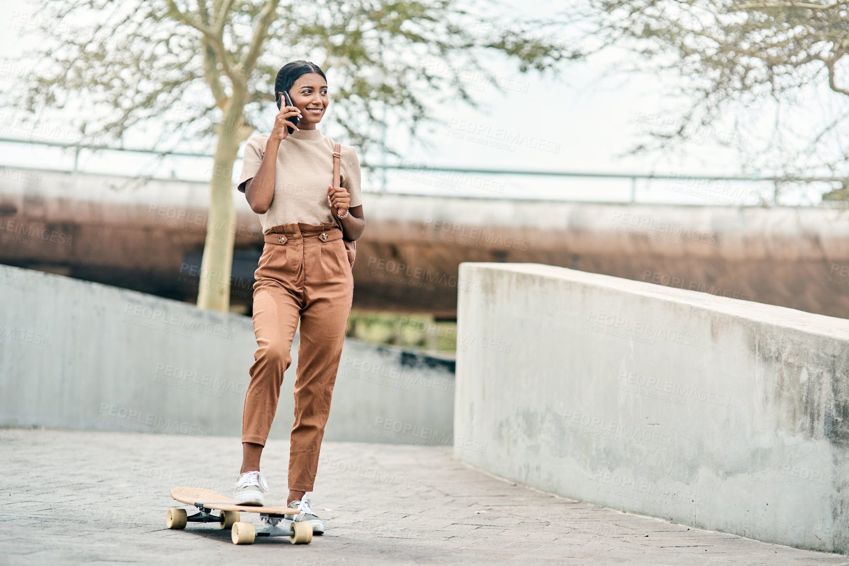 Buy stock photo Shot of an attractive young female student using her mobile phone while skateboarding on campus