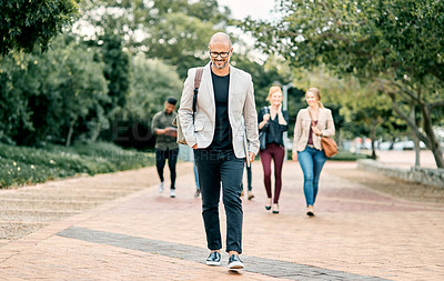 Buy stock photo Shot of a confident mature businessman walking through the city with a young team behind him