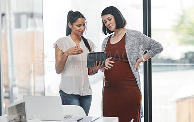 Buy stock photo Shot of a pregnant young businesswoman using a digital tablet during a meeting with her colleague in a modern office