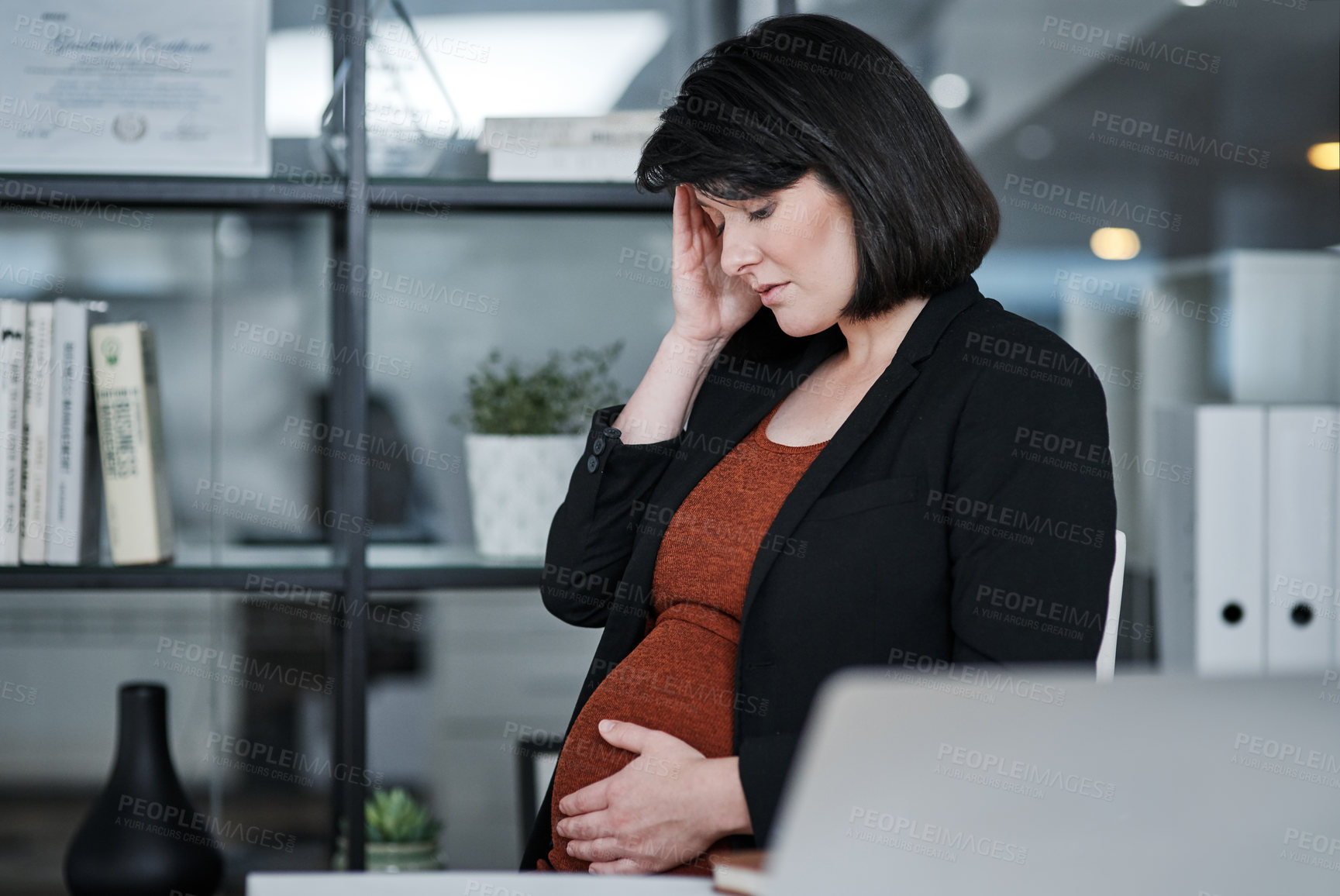 Buy stock photo Cropped shot of an attractive businesswoman sitting and feeling stressed while holding her pregnant tummy in the office