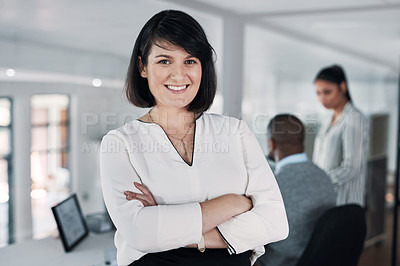 Buy stock photo Cropped shot of an attractive young businesswoman standing with her arms folded while colleagues works behind her