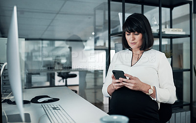 Buy stock photo Cropped shot of an attractive pregnant businesswoman sitting alone in the office and using her cellphone