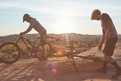 Buy stock photo Full length shot of two young male athletes mountain biking in the wilderness