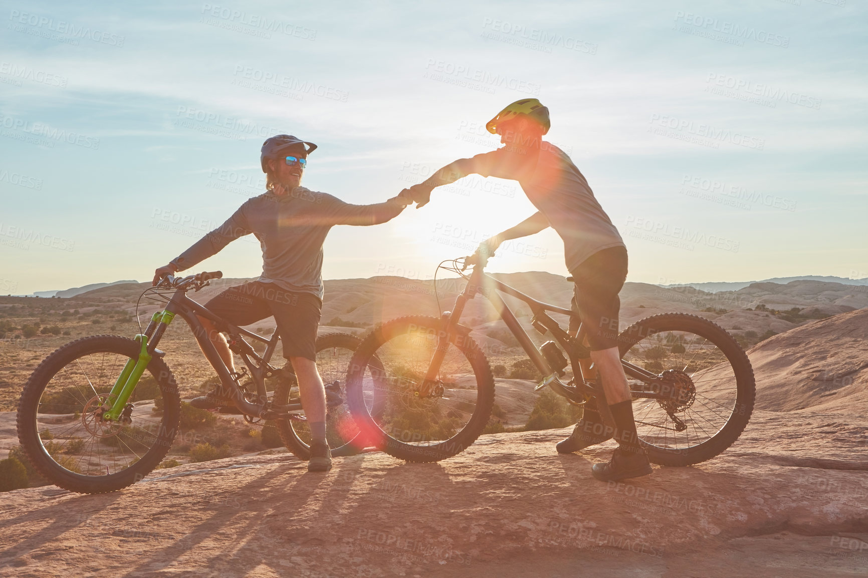 Buy stock photo Full length shot of two young male athletes fist bumping while mountain biking in the wilderness