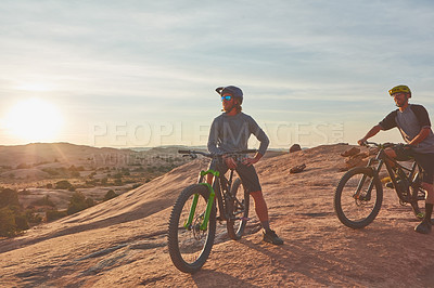 Buy stock photo Full length shot of two young male athletes mountain biking in the wilderness