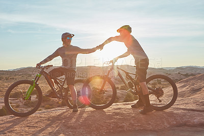 Buy stock photo Full length shot of two young male athletes fist bumping while mountain biking in the wilderness