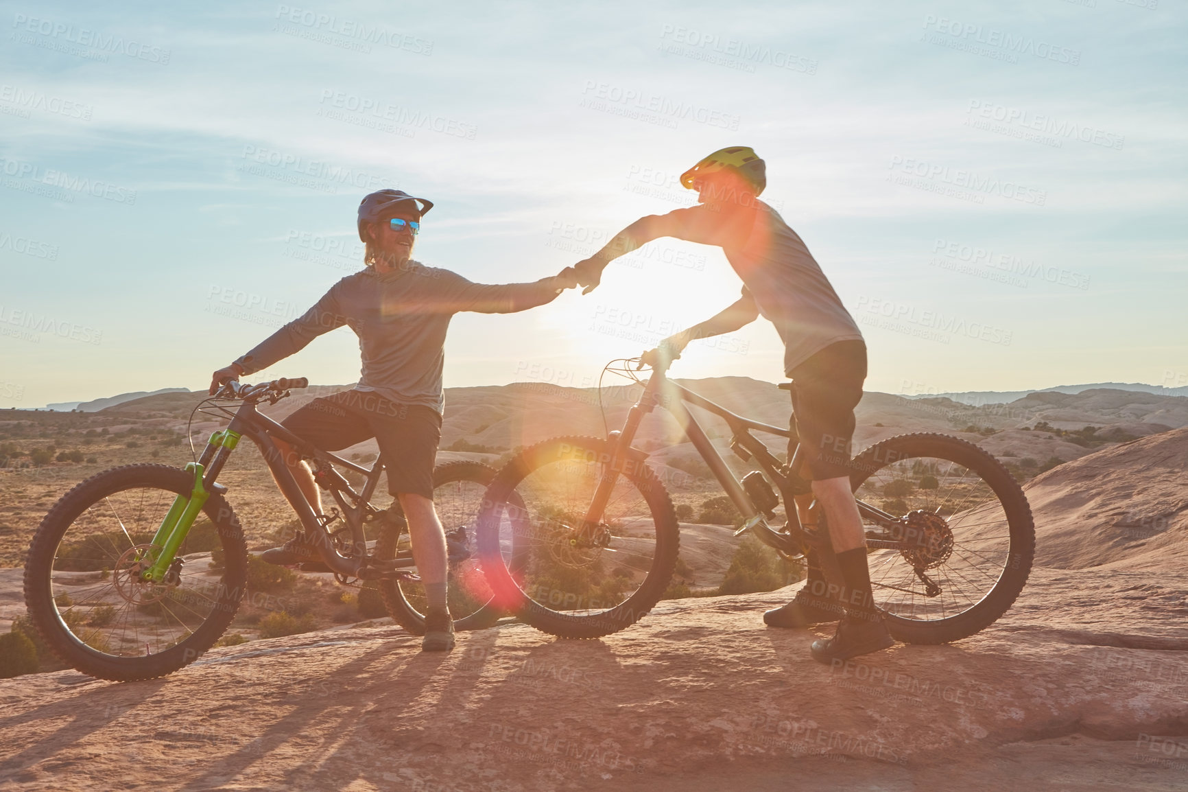 Buy stock photo Full length shot of two young male athletes fist bumping while mountain biking in the wilderness