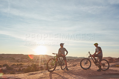 Buy stock photo Full length shot of two young male athletes mountain biking in the wilderness