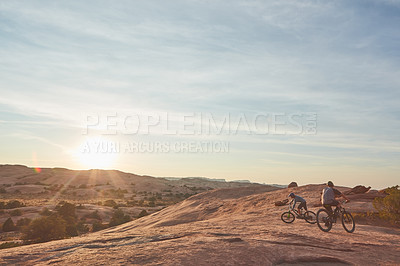 Buy stock photo Full length shot of two young male athletes mountain biking in the wilderness