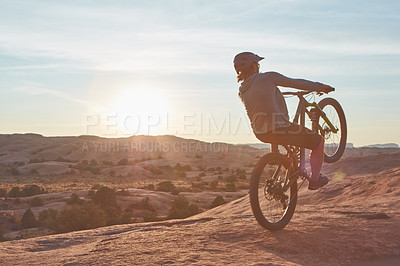 Buy stock photo Full length shot of a young male athlete popping a wheelie while mountain biking in the wilderness