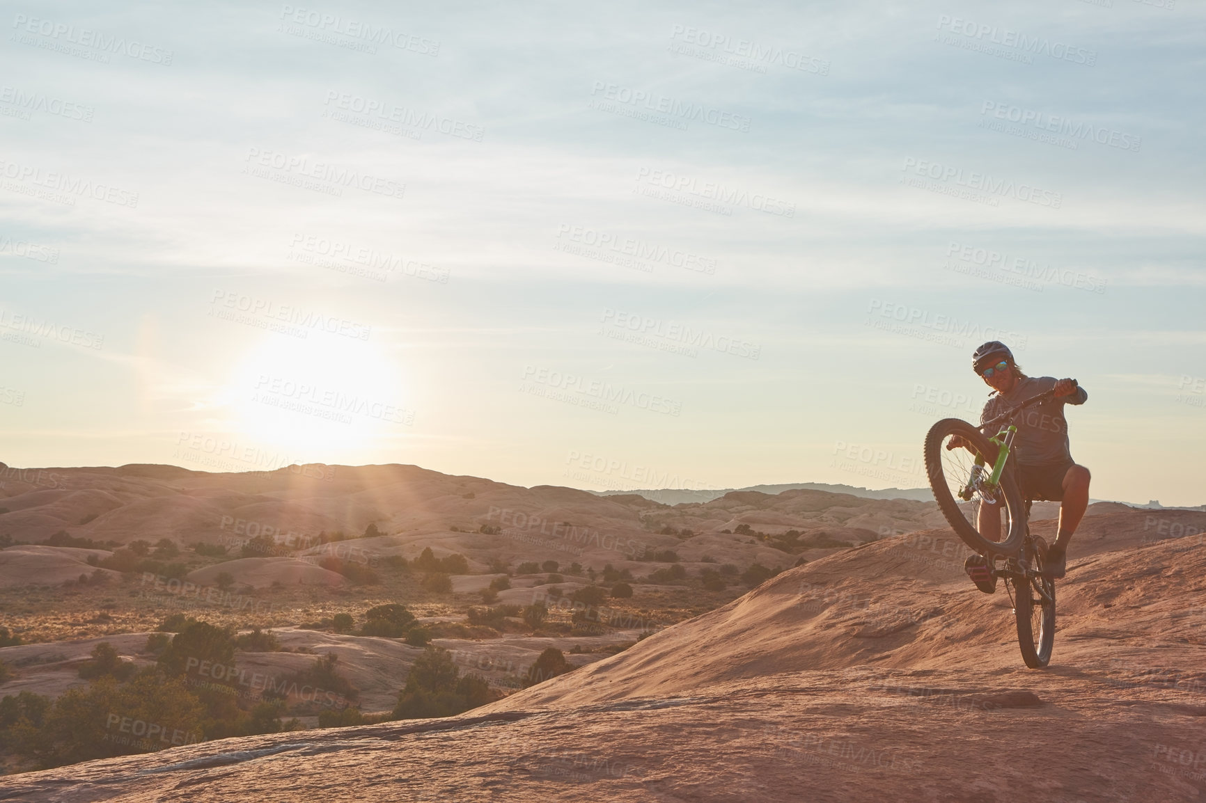 Buy stock photo Full length shot of a young male athlete popping a wheelie while mountain biking in the wilderness