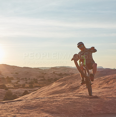 Buy stock photo Full length shot of a young male athlete popping a wheelie while mountain biking in the wilderness