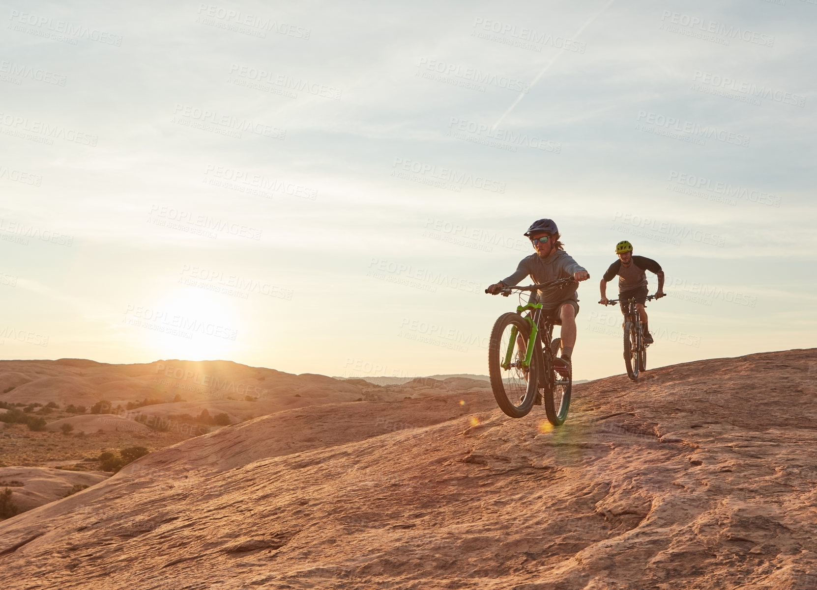 Buy stock photo Full length shot of two young male athletes mountain biking in the wilderness