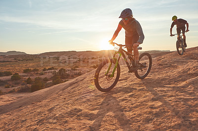 Buy stock photo Full length shot of two young male athletes mountain biking in the wilderness