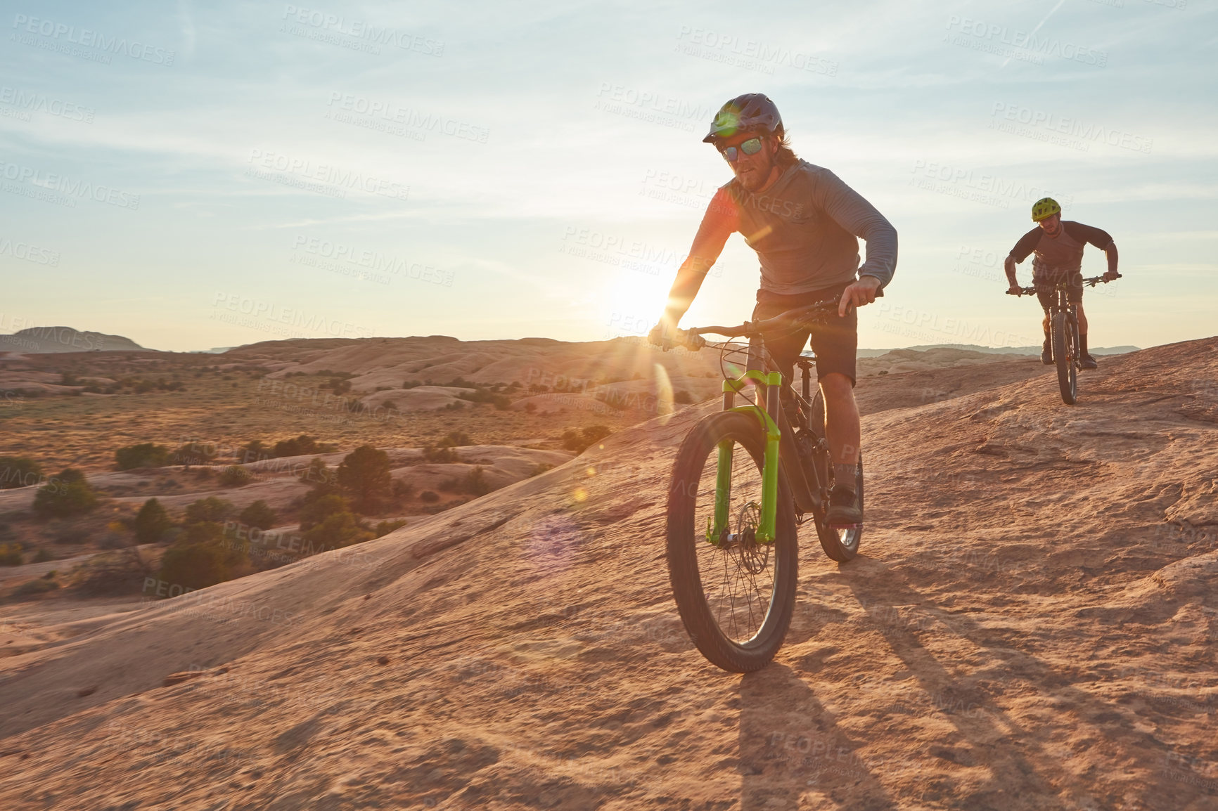 Buy stock photo Full length shot of two young male athletes mountain biking in the wilderness