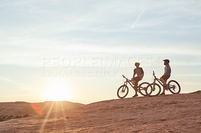 Buy stock photo Full length shot of two young male athletes mountain biking in the wilderness