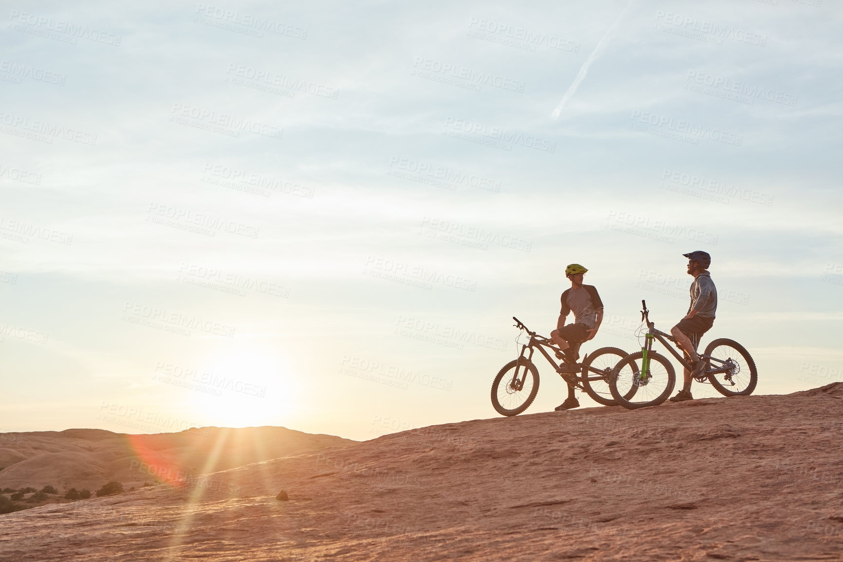 Buy stock photo Full length shot of two young male athletes mountain biking in the wilderness