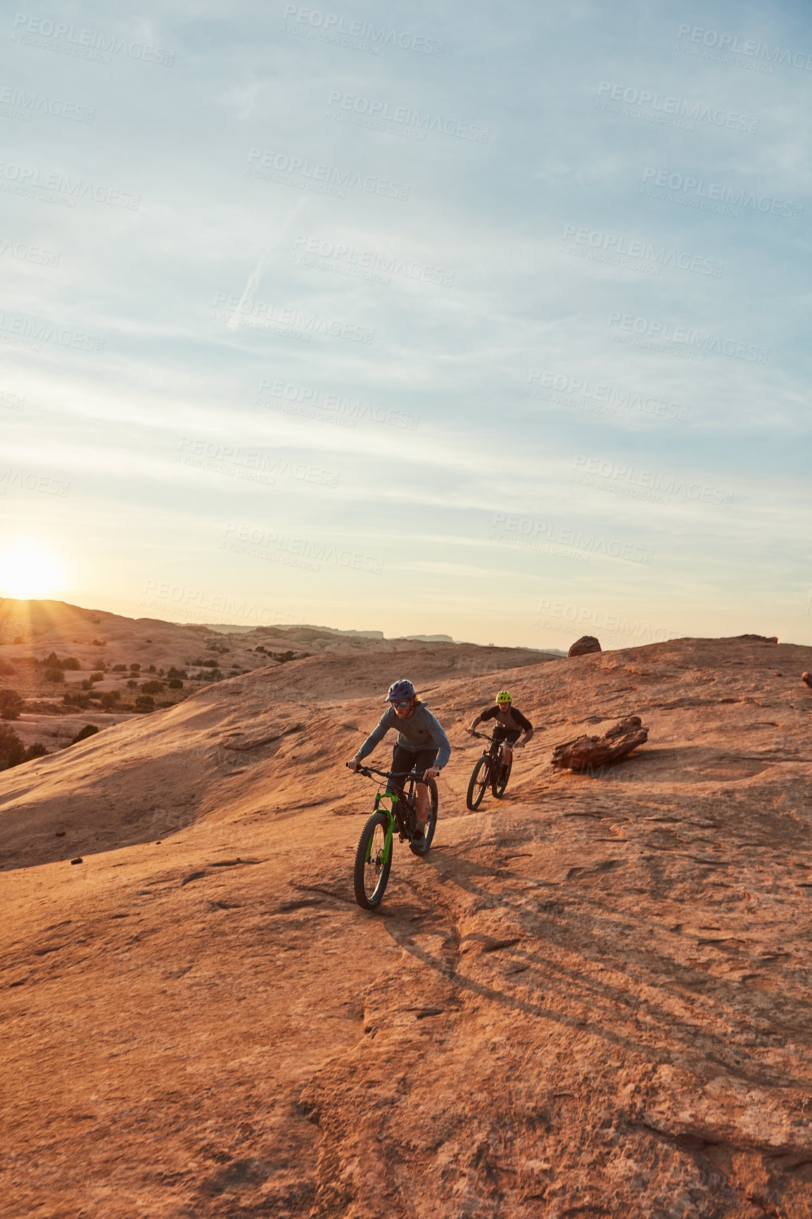 Buy stock photo Full length shot of two young male athletes mountain biking in the wilderness