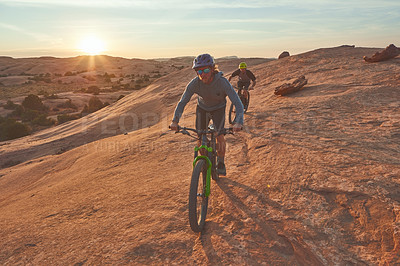 Buy stock photo Full length shot of two young male athletes mountain biking in the wilderness