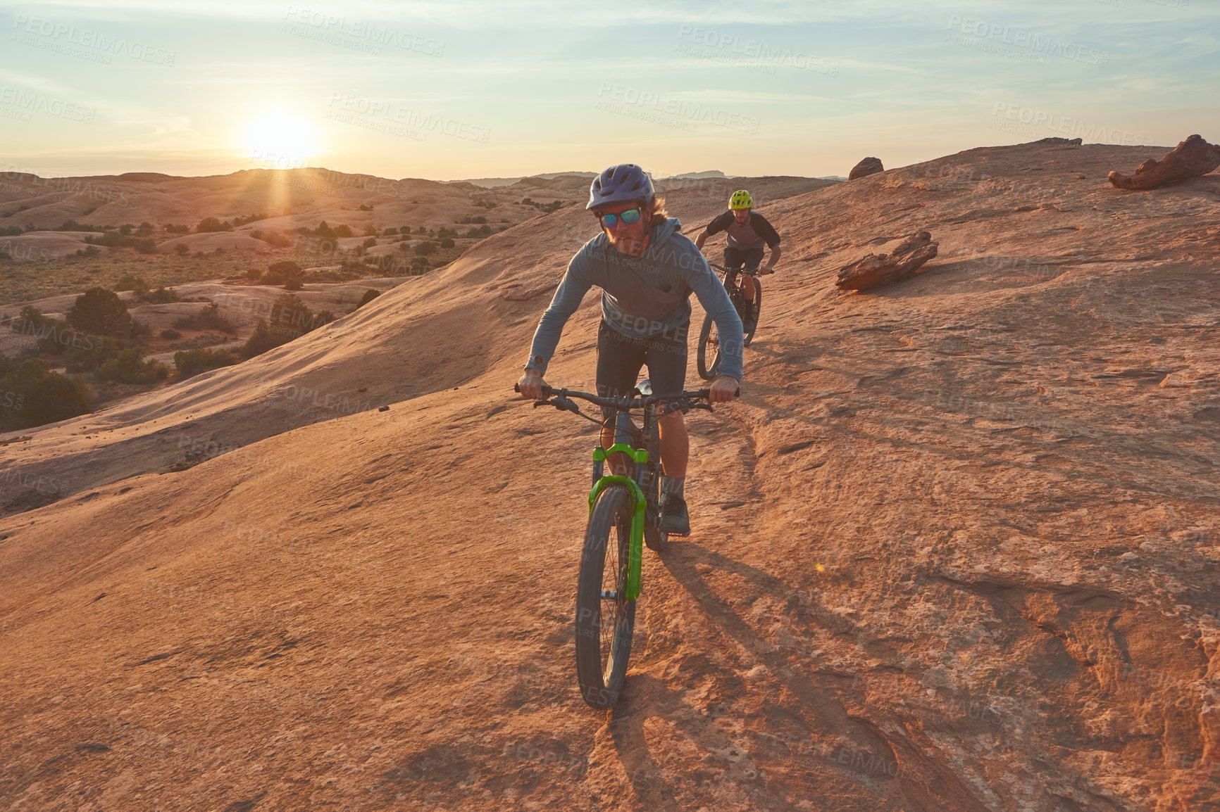 Buy stock photo Full length shot of two young male athletes mountain biking in the wilderness