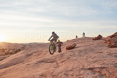 Buy stock photo Full length shot of two young male athletes mountain biking in the wilderness