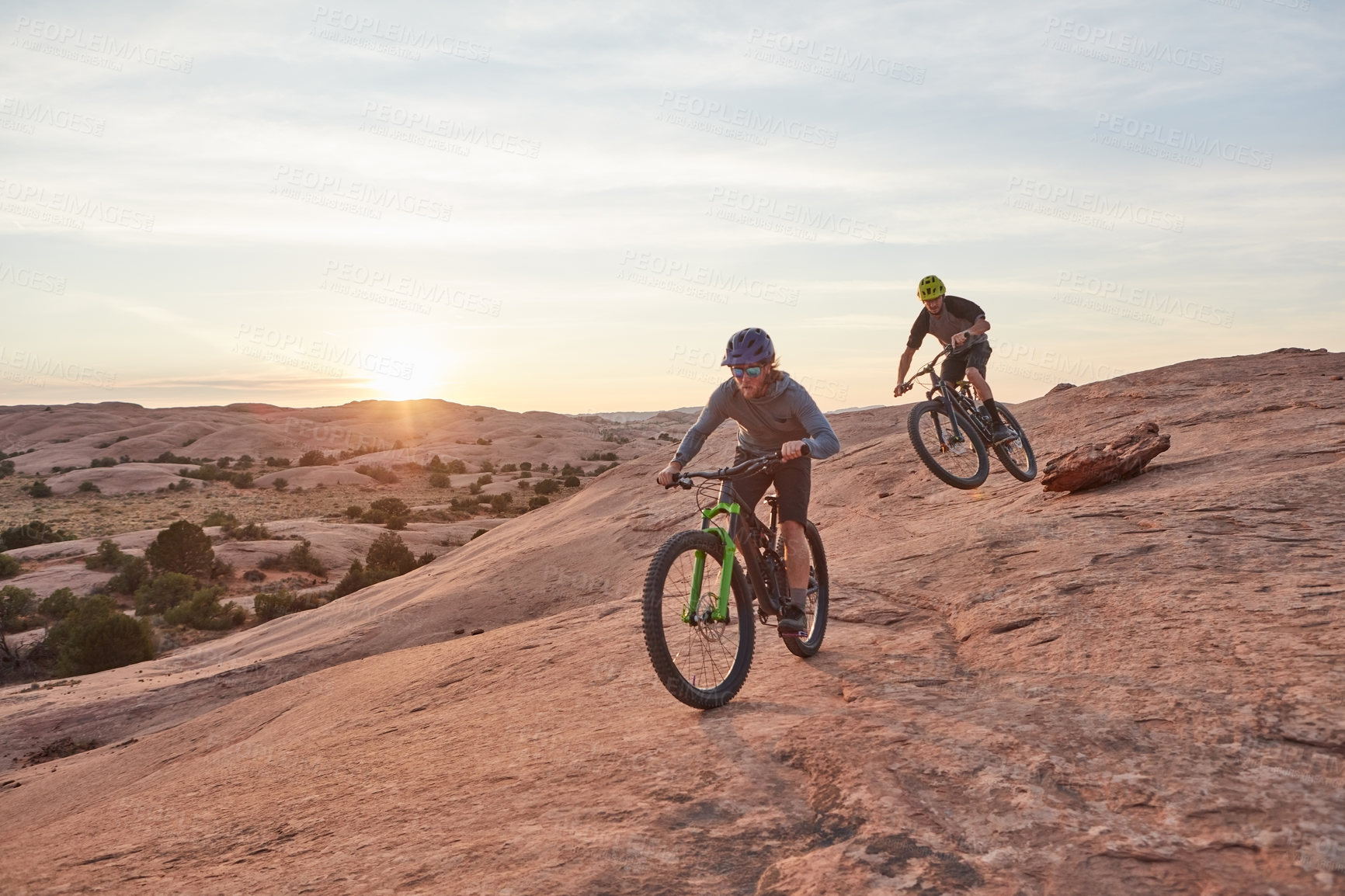 Buy stock photo Full length shot of two young male athletes mountain biking in the wilderness