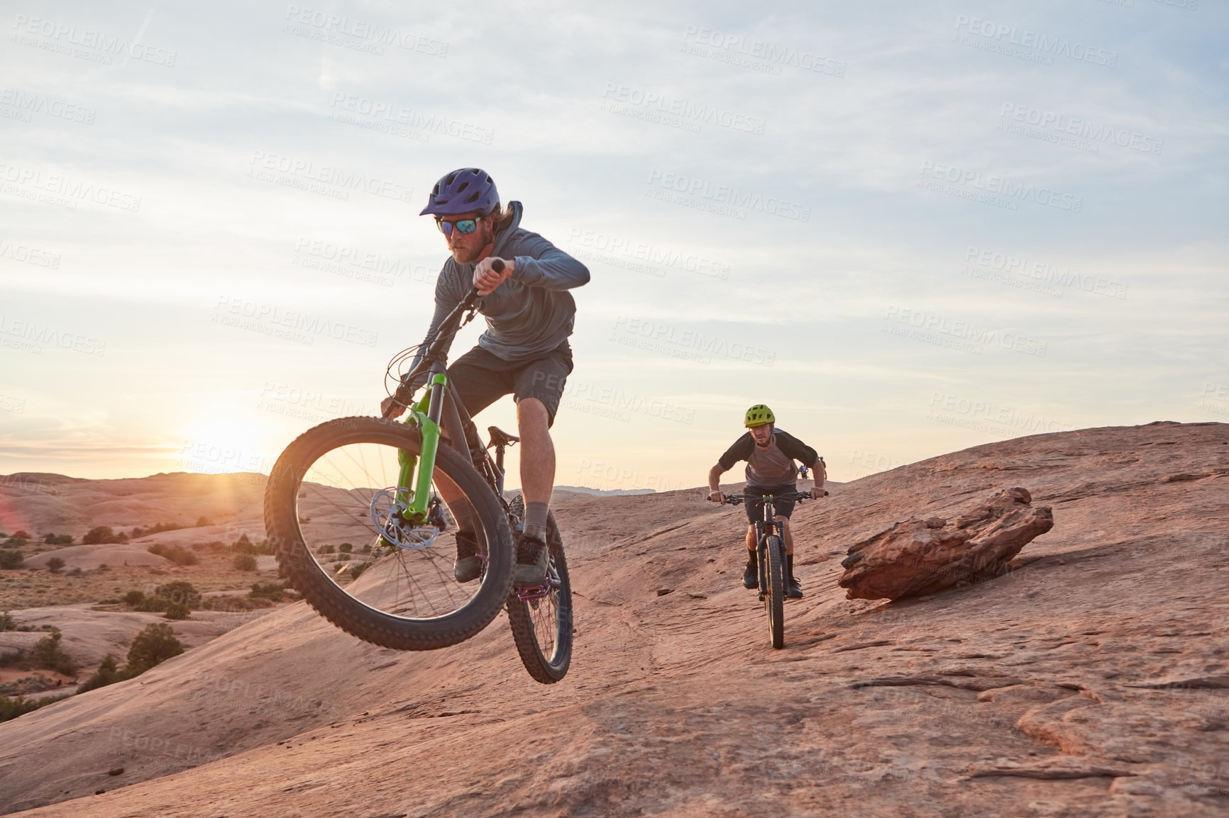 Buy stock photo Full length shot of two young male athletes mountain biking in the wilderness