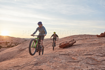 Buy stock photo Full length shot of two young male athletes mountain biking in the wilderness