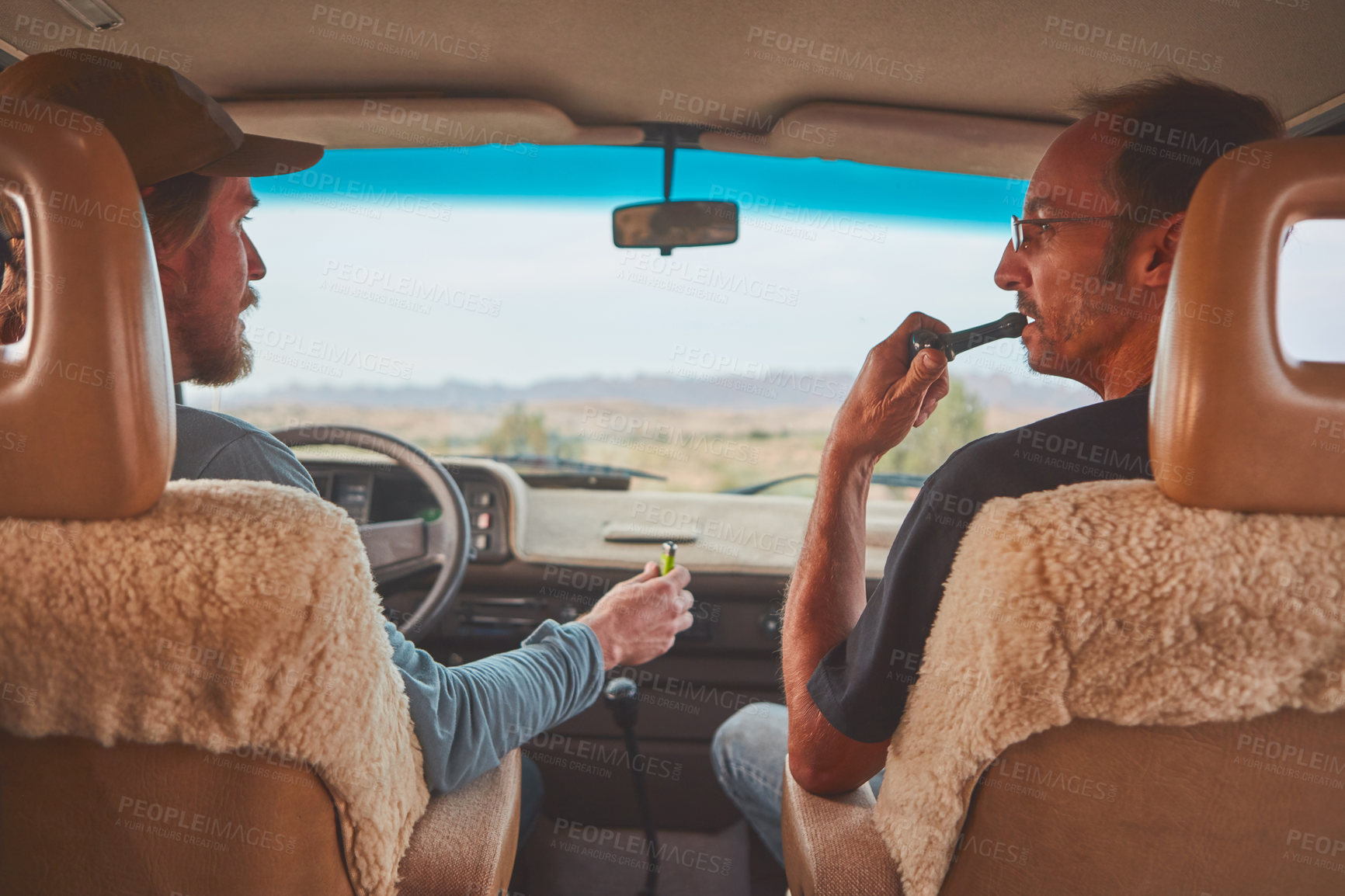 Buy stock photo Shot of two men smoking together while out on a road trip