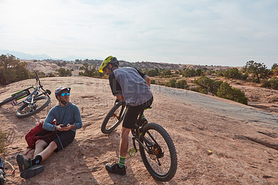 Buy stock photo Full length shot of two athletic men taking a break while mountain biking through the wilderness