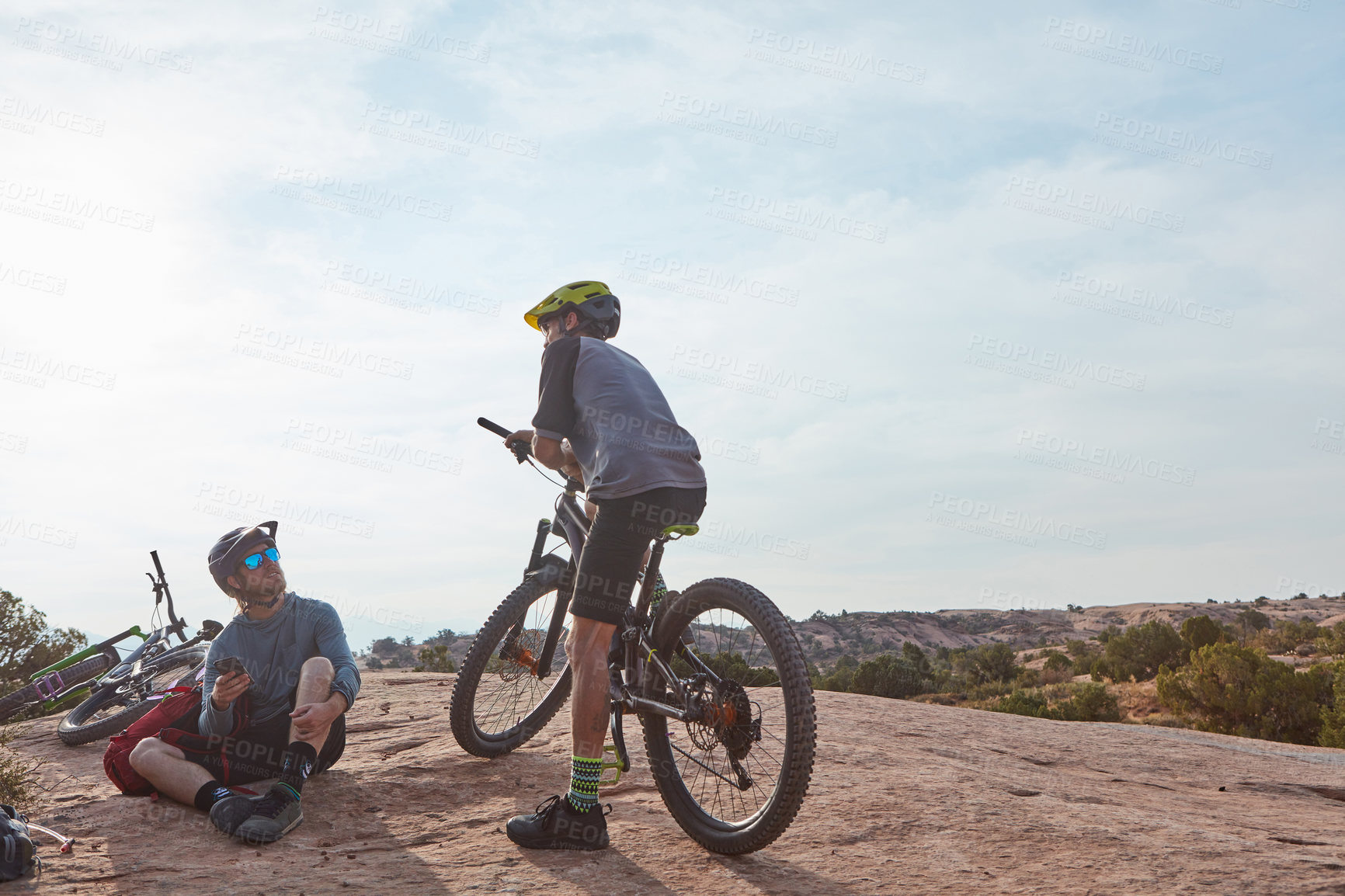 Buy stock photo Full length shot of two athletic men taking a break while mountain biking through the wilderness