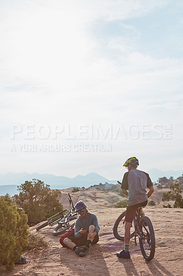 Buy stock photo Full length shot of two athletic men taking a break while mountain biking through the wilderness