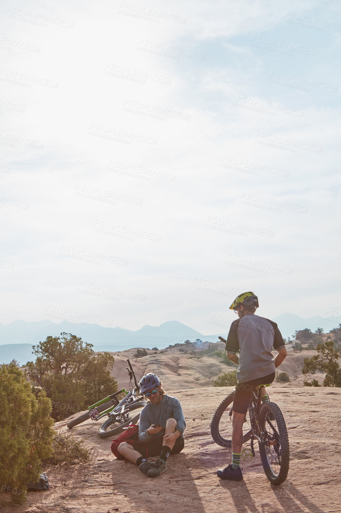 Buy stock photo Full length shot of two athletic men taking a break while mountain biking through the wilderness