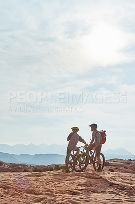 Buy stock photo Full length shot of two athletic men taking a break to admire the view while mountain biking through the wilderness