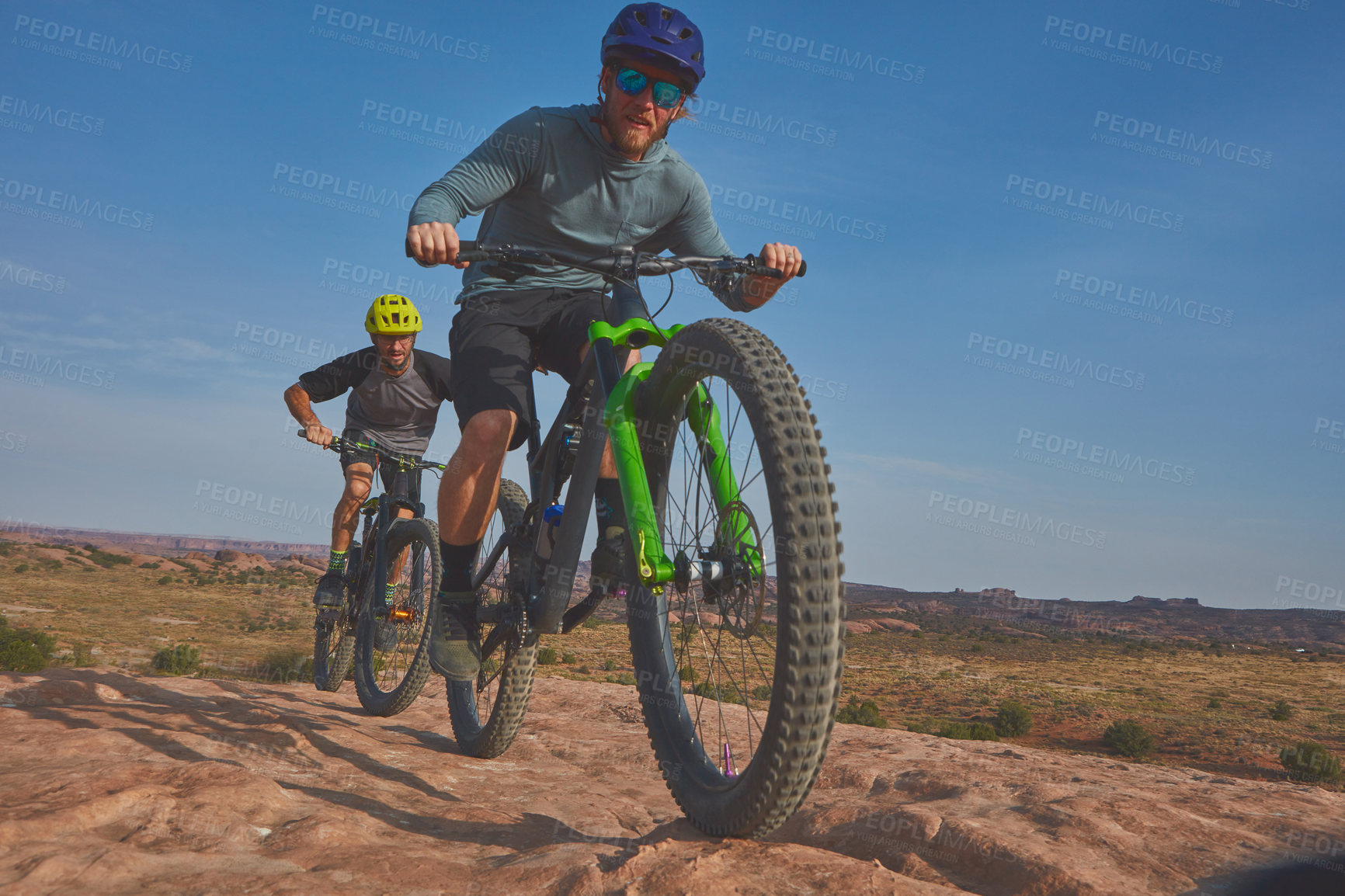 Buy stock photo Full length shot of two athletic men mountain biking through the wilderness