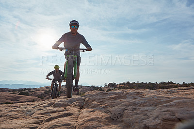 Buy stock photo Full length shot of two athletic men mountain biking through the wilderness