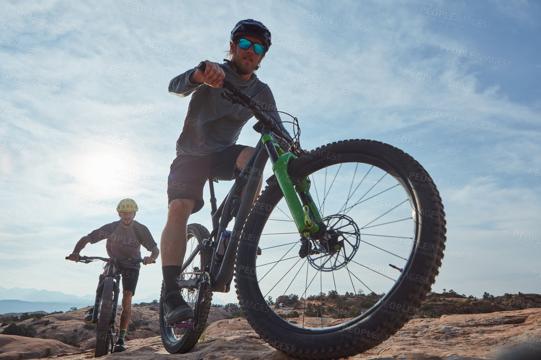 Buy stock photo Full length shot of two athletic men mountain biking through the wilderness