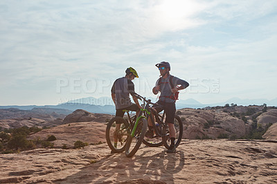 Buy stock photo Full length shot of two athletic men taking a break to admire the view while mountain biking through the wilderness