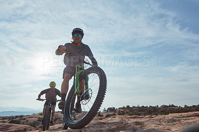 Buy stock photo Full length shot of two athletic men mountain biking through the wilderness