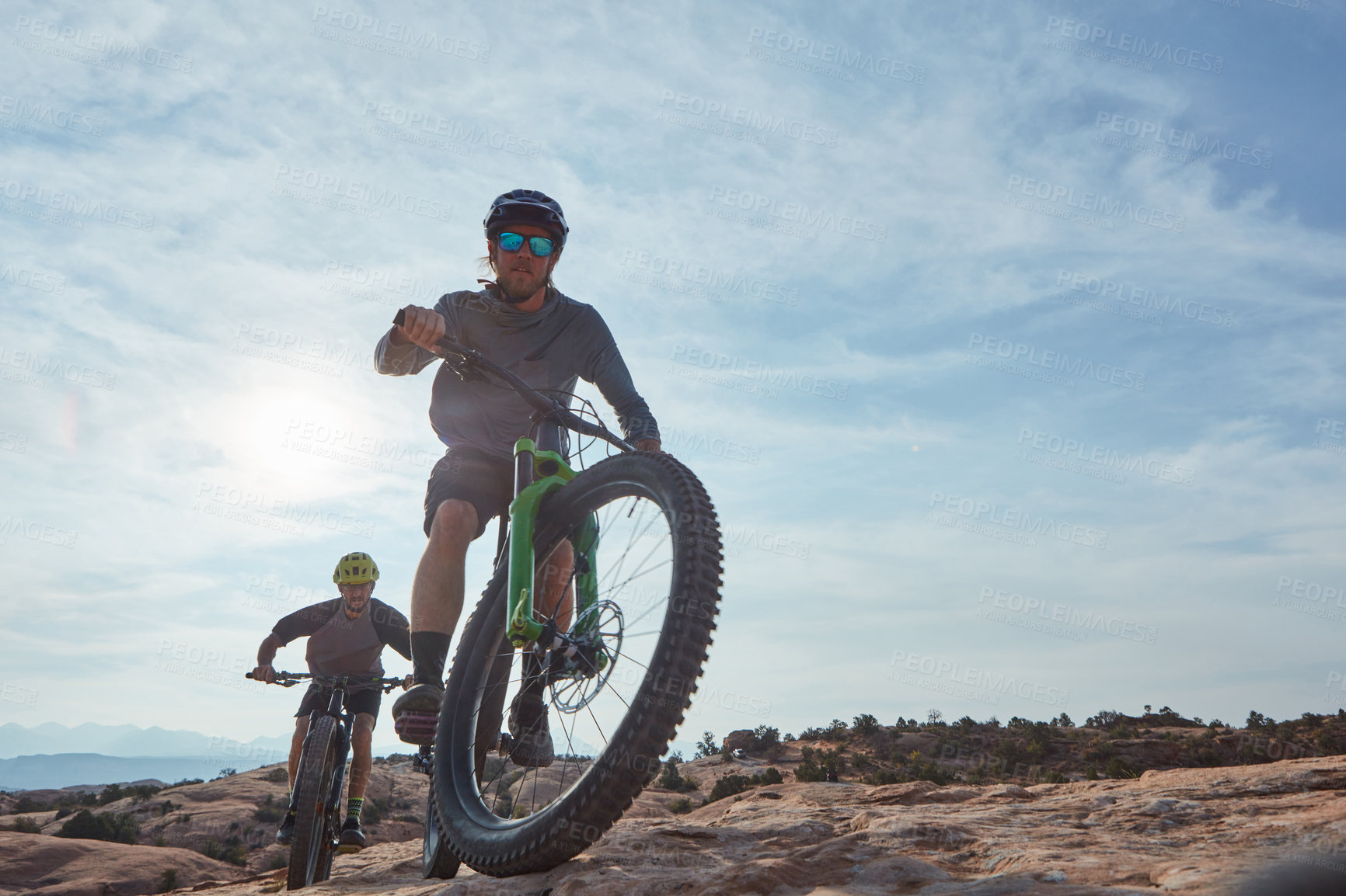 Buy stock photo Full length shot of two athletic men mountain biking through the wilderness