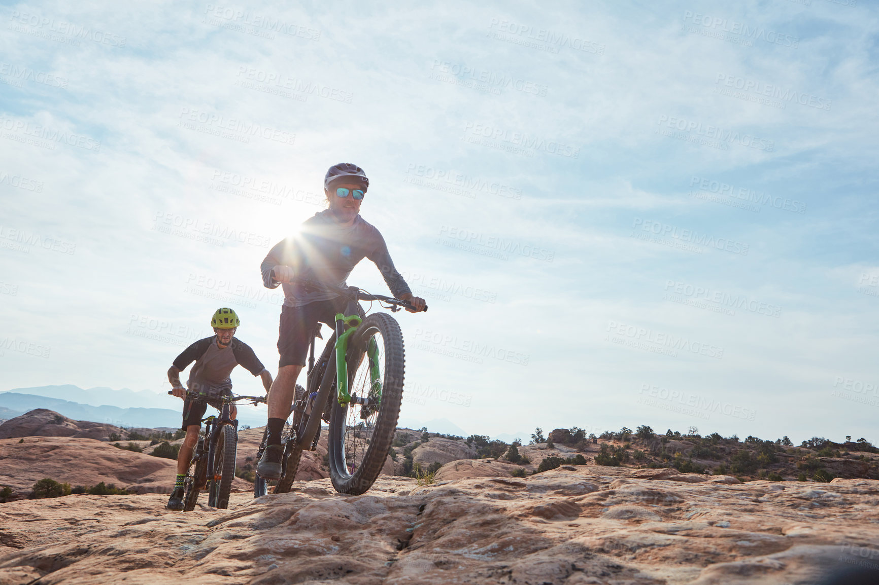 Buy stock photo Full length shot of two athletic men mountain biking through the wilderness